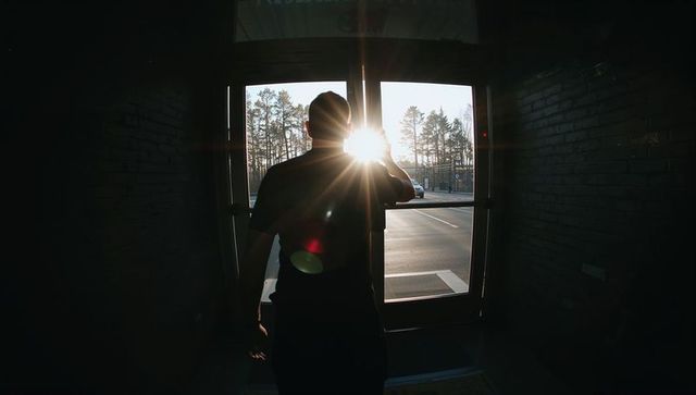 Silhouette man standing in glass doorway at sunrise with dramatic lens flare and solitude