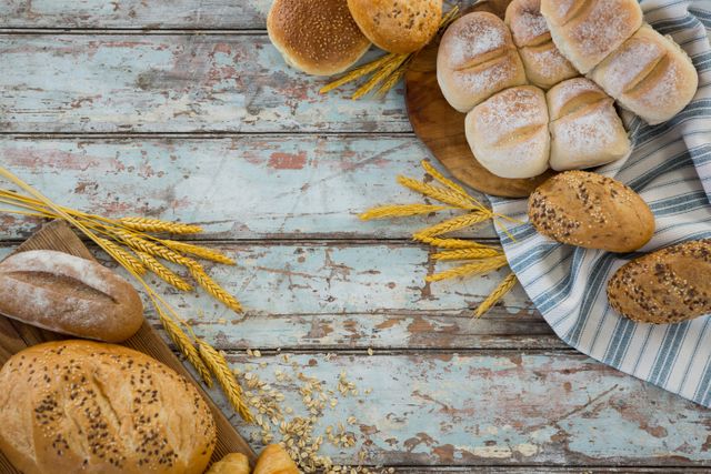 Assorted fresh bread including loaves and rolls displayed on a rustic wooden table with wheat grains. Ideal for use in bakery promotions, food blogs, recipe websites, and advertisements for organic or homemade products.