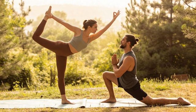 Outdoor partner yoga golden hour — woman practicing dancer pose while man holding low lunge