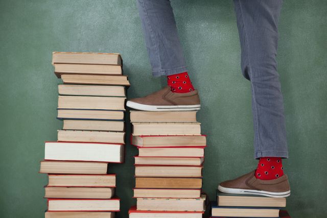 Low-section of schoolboy climbing steps of books stack against chalkboard
