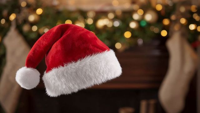 Floating Red Santa Hat Over Cozy Fireplace Mantel with Glowing Garland Bokeh Lights