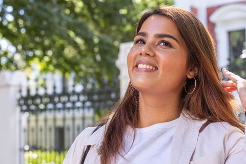 African american woman smiling on sunny urban sidewalk wearing hoop earrings and jacket