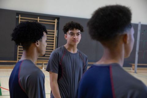 Diverse teen male teammates standing on indoor volleyball court wearing athletic shirts