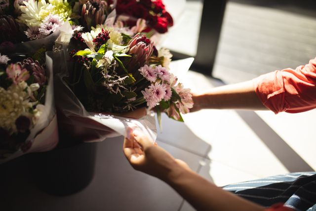 Cropped hands of biracial young female owner arranging flower bouquets on table in cafe. unaltered, cafeteria, occupation, preparation and small business concept.