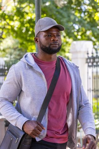 Urban commuter walking with crossbody messenger bag on sunlit tree-lined sidewalk
