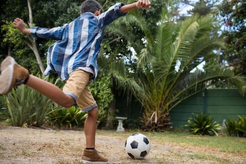 Young Boy Kicking Soccer Ball Outdoors in Backyard with Lush Greenery
