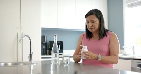 Woman holding pump bottle and wearing smartwatch at bright modern kitchen island