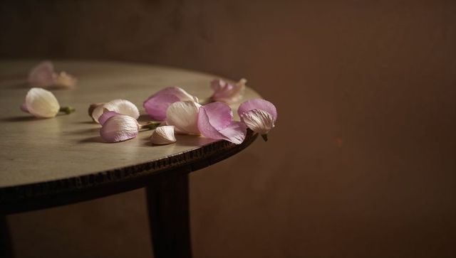 Falling pale pink petals on worn wooden round table in warm natural light
