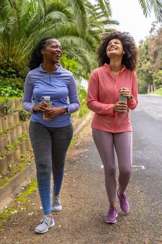 African american women walking park trail in activewear hydrating and laughing