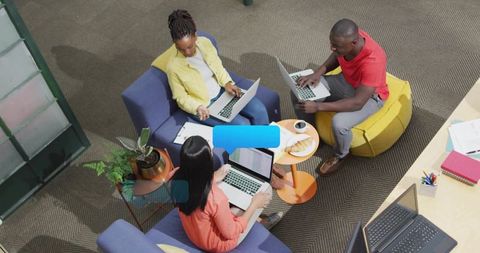 Young team collaborating in modern coworking lounge with laptops, coffee, notes, planning