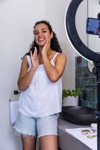 African american creator recording skincare routine with ring light and smartphone at vanity