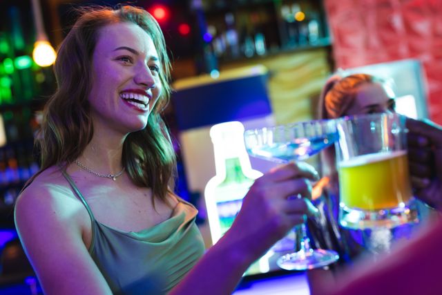 Woman smiling and holding drinks in a lively club environment. Perfect for use in content related to nightlife, social events, parties, and entertainment. Ideal for promoting bars, clubs, and social gatherings.