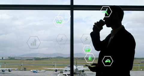 Businessman sipping coffee and checking phone at airport window with eco aviation icons