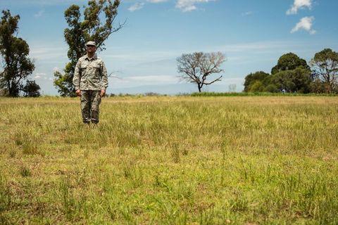 Solitary soldier standing in camouflage uniform on expansive grassland under calm blue sky