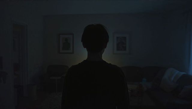 Silhouetted man standing in dim living room backlit by halo, moody introspective solitude
