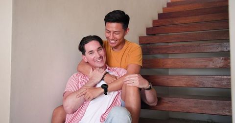 Happy Diverse Male Couple Relaxing on Wooden Stairs at Home