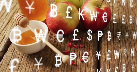 Honey apples and pomegranate seeds overlaid with floating currency symbols for food economy