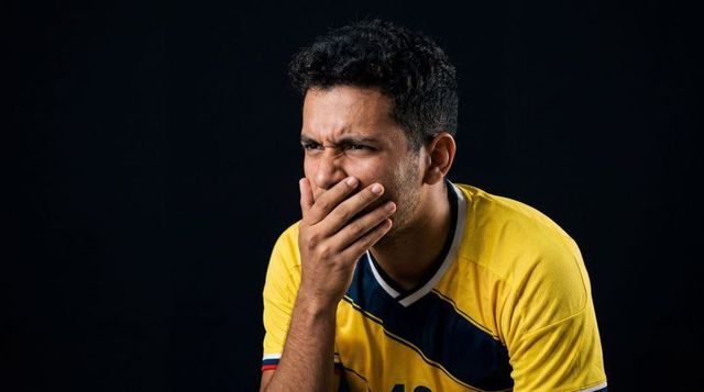 Anxious soccer fan covering mouth in yellow jersey reacting to tense match moment