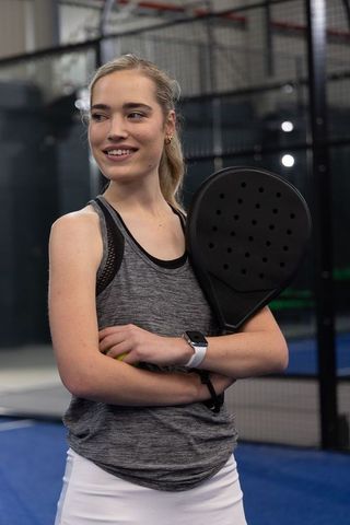Smiling female player holding padel racket and ball on indoor court wearing activewear
