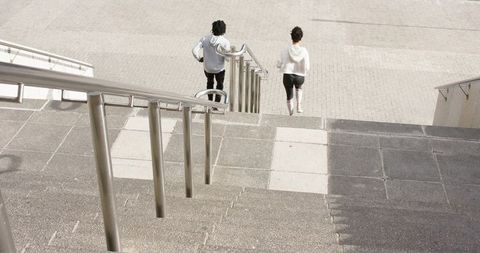 Urban friends walking down concrete stairs with stainless handrails, minimalist plaza mood
