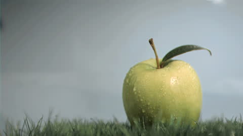Green Apple with Dew Droplets on Lawn in Slow Motion