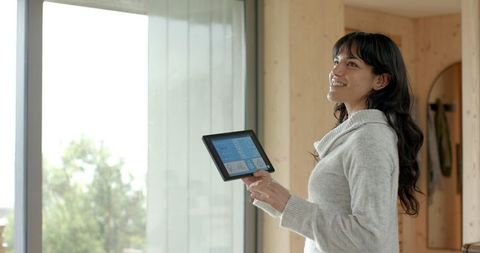 Woman using tablet for smart home automation near large window