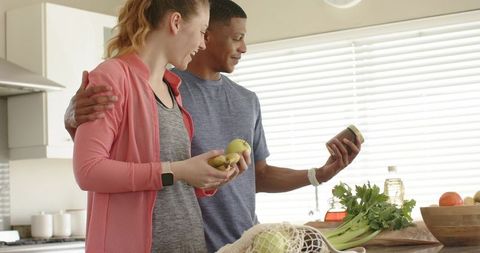 Couple unpacking groceries in modern kitchen wearing activewear and smartwatches