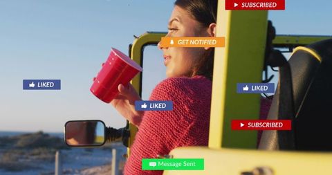 Woman holding red cup leaning out of yellow jeep on coastal dunes with social alerts