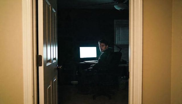 Late-night remote worker typing at home desk with glowing monitor seen through doorway