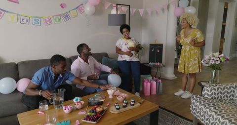 Friends Celebrating Indoor Baby Shower Gender Reveal with Pastel Decorations and Gifts