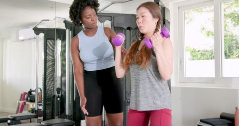 Woman exercising with fitness trainer and dumbbells in gym