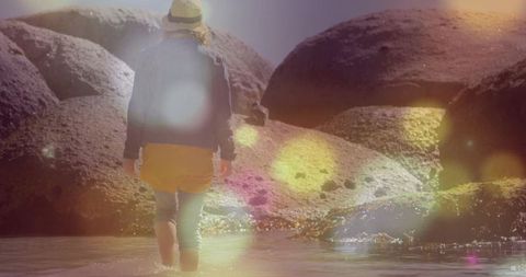 Woman wading in water near coastal boulders
