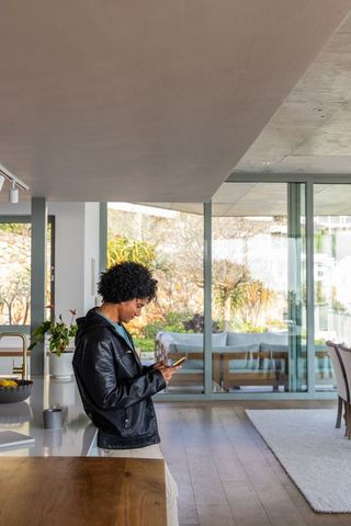 African american man leaning on kitchen island checking smartphone in modern home interior