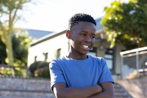 African american teen standing confidently with arms crossed smiling in sunlit neighborhood