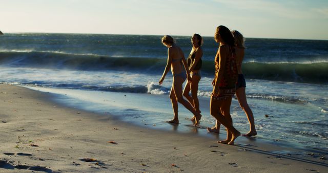 Four women enjoying a walk along a sandy beach with ocean waves in the background during sunset. Perfect for themes related to summer vacations, leisure, friendship, outdoor activities, and nature. Ideal for travel blogs, tourism advertisements, or social media posts promoting a relaxing and picturesque beach experience.