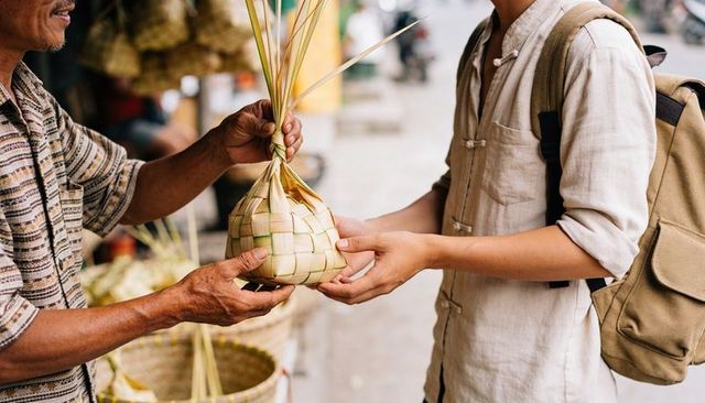 Senior vendor handing woven palm-leaf basket to backpacking customer at street market
