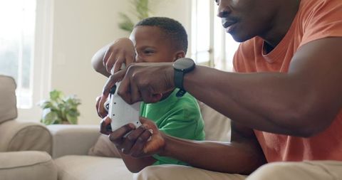 African American Father Teaching and Bonding with Son Through Console Gaming on Sofa