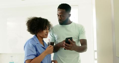 African American Couple Brushing Teeth While Checking Smartphone in Morning Bathroom Routine