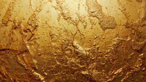 Slow-moving camera revealing textured gilded surface with embossed relief and liquid droplets
