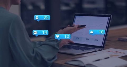 Mid-adult woman pointing at laptop analytics with social notification bubbles in office
