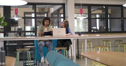 African american colleagues collaborating at coworking bar pointing at notebook and laptop