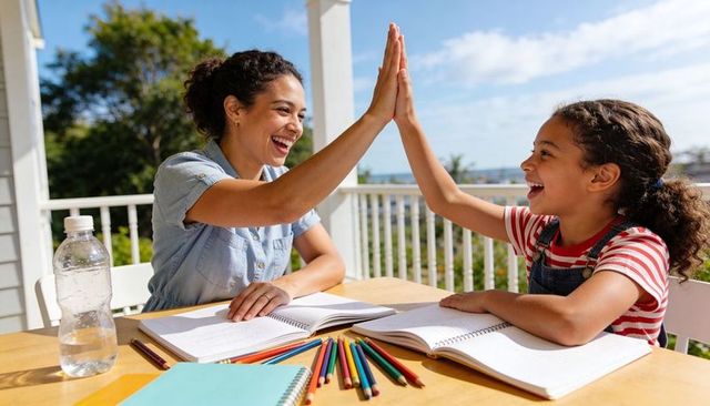 Smiling tutor and child high-fiving on sunny porch during outdoor home learning session