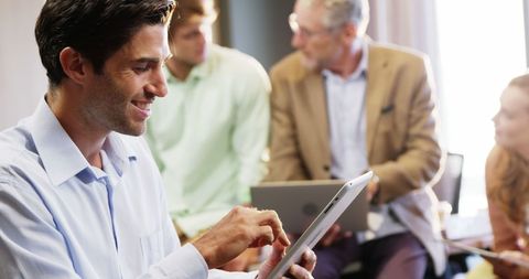 Businessman Engaged with Digital Tablet During Collaborative Office Meeting - Download Free Stock Images Pikwizard.com