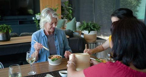 Multigenerational women sharing asian meal at home using bamboo steamer and chopsticks