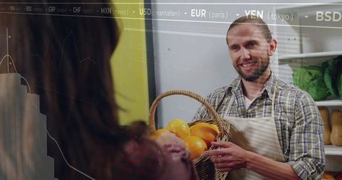Friendly market vendor handing basket of oranges to customer at bustling farm stand