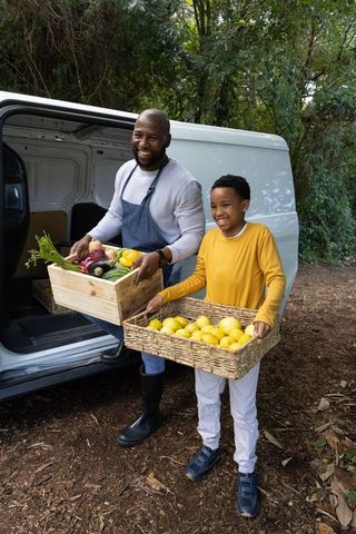 African american father and son carrying fresh produce from van smiling at rural market