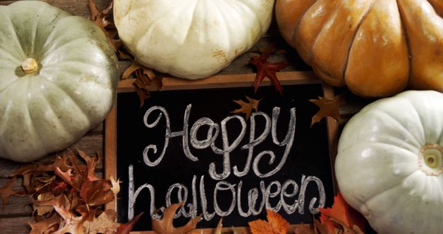 Chalkboard with 'Happy Halloween' written in chalk surrounded by various pumpkins and fallen autumn leaves. Suitable for seasonal greetings, social media posts, blog articles about Halloween, and festive party invitations.