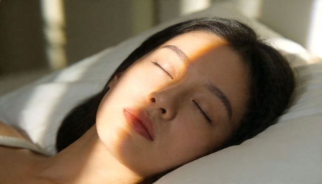 Sunlit asian woman resting on pillow with serene expression and sunbeam across face