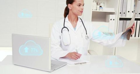 Female doctor inspecting x-ray while using laptop with cloud medical data icons