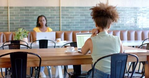 Working in modern cafe coworking space with laptops and coffee by focused women with natural light